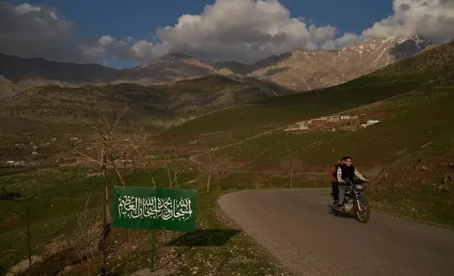 2026年3月17日，周二，在伊拉克哈拉卜賈附近山區的伊拉克-伊朗邊境附近，一名男子騎着電單車經過一個寫有阿拉伯語祈禱文「榮耀歸於真主；偉大的真主，榮耀歸於祢」的標誌。(美聯社圖片/利奧·科雷亞) AP圖片