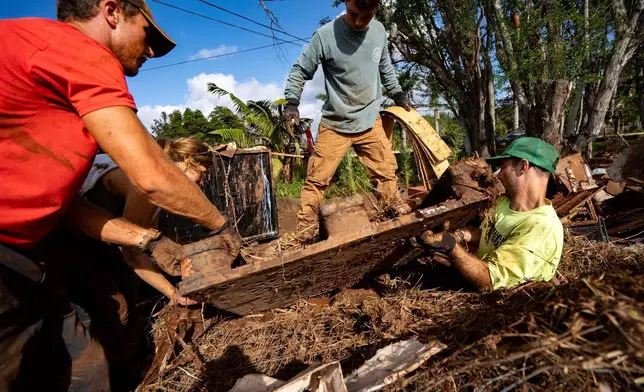 2026年3月24日周二，居民凱布里·瓊斯（Kaybri Jones，左）和安東尼·斯卡拉（Anthony Scala），以及志願者在夏威夷哈雷瓦（Haleiwa）的一個臨時垃圾堆放場清理泥濘的碎片。(美聯社圖片/Mengshin Lin) AP圖片