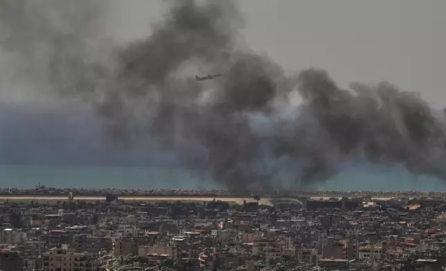 2026年3月17日周二，一架中東航空的飛機從拉菲克哈里里國際機場起飛，同時黎巴嫩貝魯特南部郊區達希耶的以色列空襲現場冒出濃煙。(美聯社圖片/Hassan Ammar) AP圖片