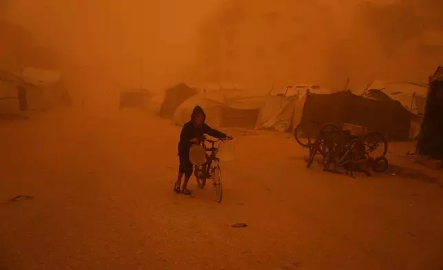 2026年3月14日周六，在加沙地帶南部的汗尤尼斯（Khan Younis），一名男孩推著載有水壺的單車穿過沙塵暴。(美聯社圖片/Abdel Kareem Hana) AP圖片