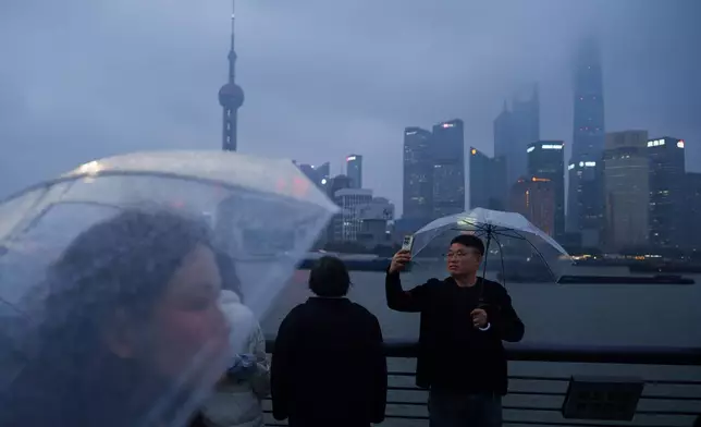 2026年3月16日周一，在上海的雨天，人們在外灘自拍，浦東的天際線隔著黃浦江可見。(美聯社圖片/Vincent Thian) AP圖片