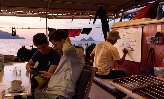 2026年3月3日周二，印尼四王群島Raja Laut潛水船上，潛水員亞歷杭德羅·薩羅（Alejandro Sarró，左）和馬內爾·桑格拉（Manel Sangrà）查看手機，潛水導遊克里斯塔托·溫布·庫杜（Kristanto Umbu Kudu）準備簡報。(美聯社圖片/Claudia Rosel) AP圖片