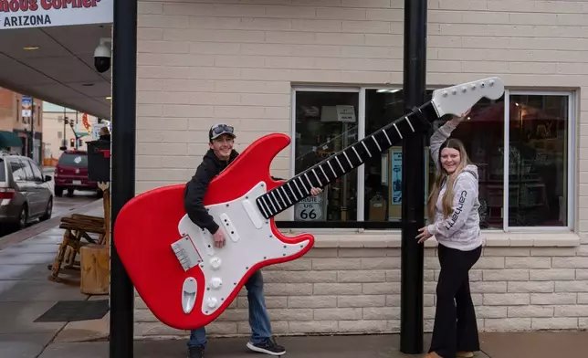 2025年11月20日（周四），新婚夫婦基思赫德伯格（Keith Hedberg，左）和妻子阿德里安娜赫德伯格（Adriana Hedberg）從堪薩斯州錫拉丘茲（Syracuse, Kansas）度蜜月，在亞利桑那州溫斯洛（Winslow, Ariz.）一間禮品店外，與一個大型結他裝置合影。該鎮位於歷史悠久的66號公路（Route 66）上。（美聯社圖片/Jae C. Hong） AP圖片