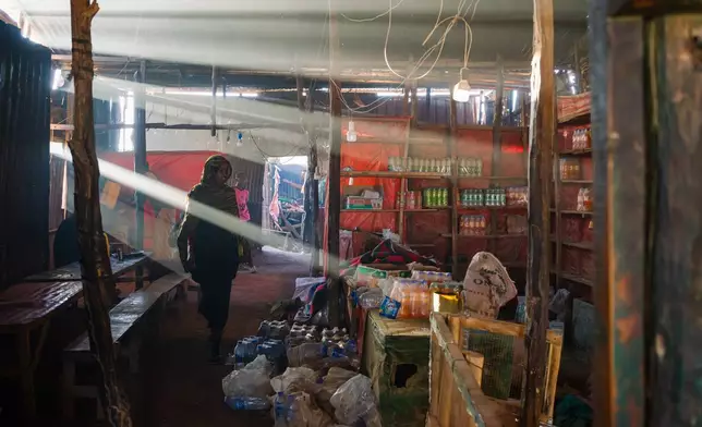 2026年1月8日周四，埃塞俄比亞阿夫卡德，在一家昏暗的路邊餐廳，燃燒沒藥（用於驅蟲驅蛇）的煙霧與煮食的煙霧混雜，一名年輕女子走過水瓶和汽水瓶旁。(美聯社圖片/Julianne Gauron) AP圖片