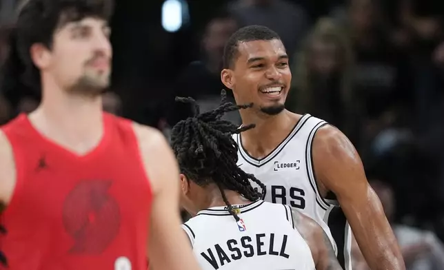 波特蘭拓荒者前鋒丹尼艾夫迪亞（Deni Avdija）（左）走過，聖安東尼奧馬刺前鋒/中鋒文班亞馬（Victor Wembanyama）（右）在2026年4月28日，周二，聖安東尼奧舉行的NBA季後賽首圈第五場比賽下半場，一次攻防後微笑。(美聯社圖片/Eric Gay) AP圖片