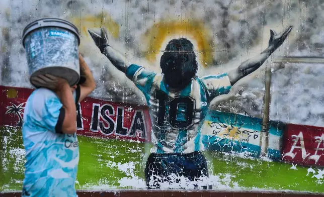 2026年4月13日周一，一名行人提著水桶走過阿根廷布宜諾斯艾利斯（Buenos Aires）一幅描繪已故足球傳奇馬勒當拿（Diego Maradona）的塗鴉。（美聯社圖片/Rodrigo Abd） AP圖片
