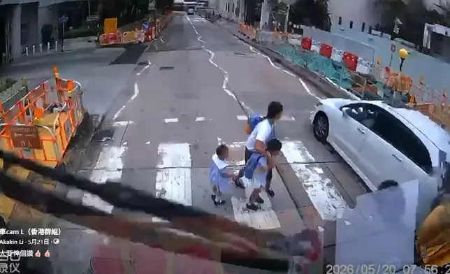 一名女傭帶着兩名身穿校服的幼童橫過斑馬線期間，一輛白色私家車逆線直衝而過，幸女傭及時拉住幼童，避過一劫。車cam L（香港群組）FB群組視頻截圖