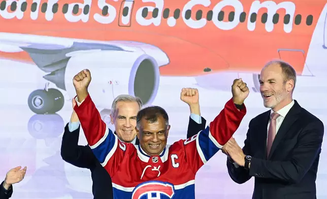 2026年5月6日周三，在魁北克（Quebec）米拉貝爾（Mirabel）的空中巴士A220交付中心一項活動上，亞洲航空（AirAsia）簽署了150架空中巴士A220客機的里程碑式訂單。圖為加拿大總理馬克卡尼（Mark Carney）（左）及空中巴士商用飛機行政總裁拉爾斯華格納（Lars Wagner）（右）為亞洲航空行政總裁東尼費南迪斯（Tony Fernandes）（中）喝采。(美聯社圖片/Graham Hughes/The Canadian Press) AP圖片