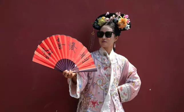 2026年4月4日周六，一名女子在北京故宮外，穿上中國歷史服飾，手持寫有「祝你幸福繁榮」字樣的扇子。(美聯社圖片/Ng Han Guan) AP圖片