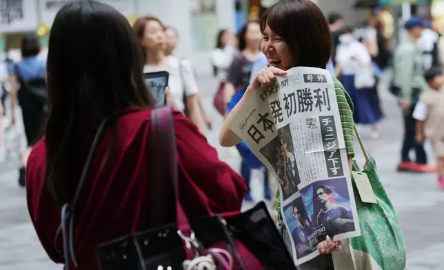 2026年6月21日周日，日本隊在墨西哥舉行的世界盃F組足球賽中擊敗突尼西亞後，一名女子在東京與讀賣新聞報社職員派發的號外合照。(美聯社圖片/Hiro Komae) AP圖片
