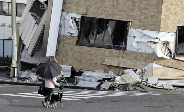 2026年7月29日周三，熊本縣八代市，人們牽狗走過一棟被地震震塌的建築物。(美聯社圖片/橫山純太郎/共同社) AP圖片
