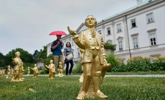 人們經過德國藝術家奧特馬爾·赫爾製作的400個金色塑膠莫扎特雕塑，這些雕塑在奧地利薩爾斯堡展出，以紀念莫扎特誕辰270周年。攝於2026年7月15日周三。(美聯社圖片/Matthias Schrader) AP圖片