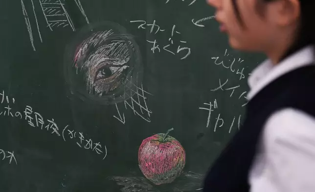 (美聯社圖片/Hiro Komae) 二零二六年七月二十一日周二，在東京西北部熊谷的熊谷女子高等學校，一名藝術學會成員走過黑板上的粉筆畫設計，她們正在討論為全國比賽準備的黑板藝術設計。 AP圖片