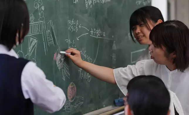 (美聯社圖片/Hiro Komae) 二零二六年七月二十一日，在東京西北部熊谷的熊谷女子高等學校，藝術教師青木（右）向藝術學會的新生展示粉筆繪畫技巧。 AP圖片