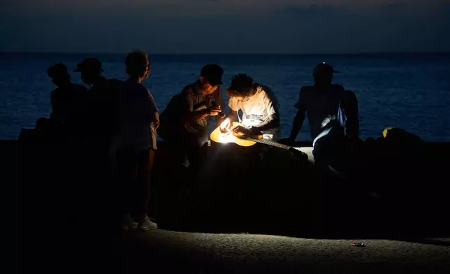 2026年7月14日周二，古巴哈瓦那，一名男子在停電期間，於馬雷貢海堤上藉手電筒燈光修理結他弦。(美聯社圖片/Ramon Espinosa) AP圖片