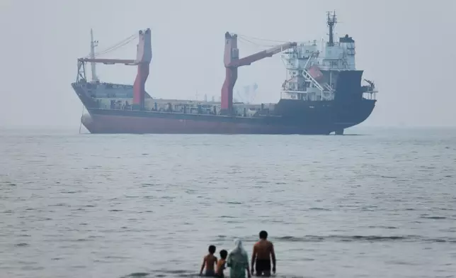 2026年6月30日周二，伊朗阿巴斯港對開的霍爾木茲海峽，一群人站在淺水中，一艘貨船停泊在海峽內。(伊朗學生通訊社圖片/美聯社/Amirhosein Khorgooi) AP圖片