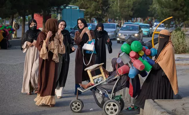 在阿富汗喀布爾街上，一群年輕女子經過一名售賣塑膠水壺的婦女，為美國撤軍及塔利班開始統治五周年作準備。攝於2026年8月14日周五。(美聯社圖片/Nava Jamshidi) AP圖片