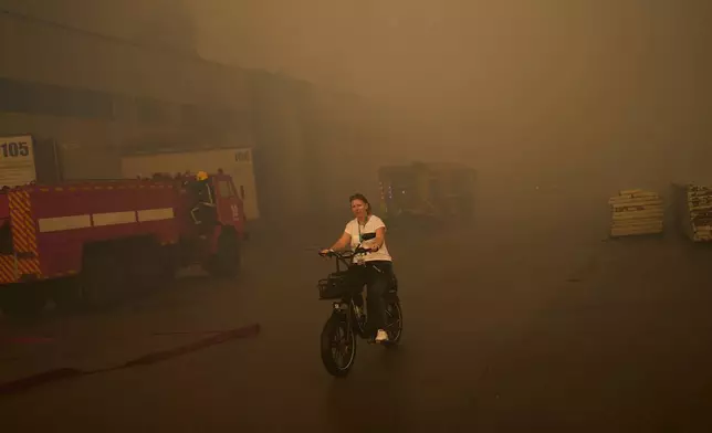 2026年9月3日周四，烏克蘭基輔市郊，俄羅斯無人機襲擊後，消防員正撲滅一個被摧毀的藥品倉庫大火，一名女子騎單車經過。(美聯社圖片/Francisco Seco) AP圖片
