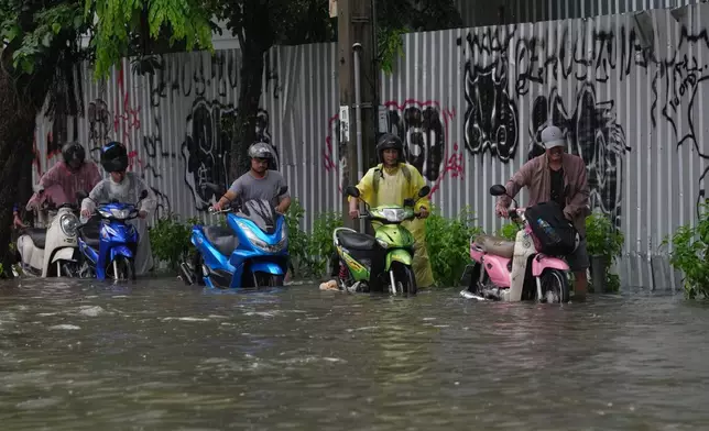 2026年9月26日周六，泰國曼谷暴雨後，多名男子推著電單車涉水而行。(美聯社圖片/Sakchai Lalit) AP圖片