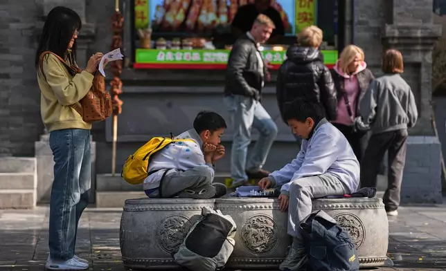 2026年10月22日周四，學生在北京前門大街的戶外學校活動期間，坐在凳上玩國際象棋。(美聯社圖片/Andy Wong) AP圖片