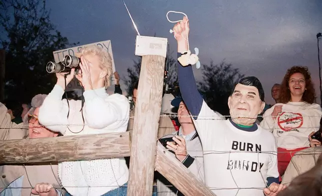 檔案圖片：1989年1月25日日出時分，在佛羅里達州斯塔克，支持死刑的人群在泰德·邦迪被處決後歡呼，亞特蘭大居民傑里·傑克遜戴着列根面具，將一個玩具兔子吊起來示眾。(美聯社圖片/Mark Foley) AP圖片