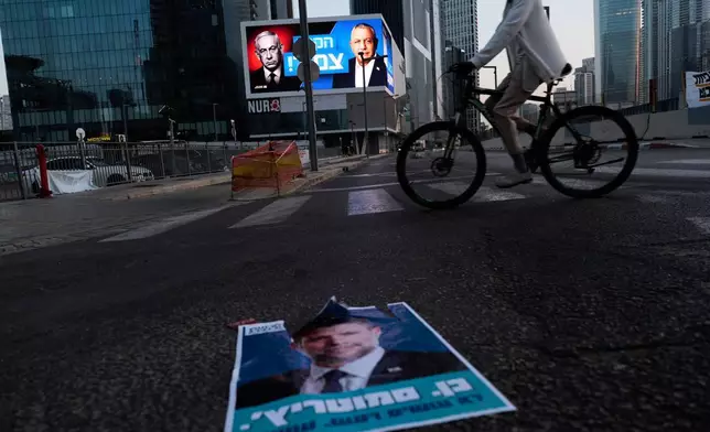 一名單車手經過一個競選廣告牌，上面印有以色列總理內塔尼亞胡（左）及其主要對手、反對派候選人加迪艾森科特，並附有希伯來文訊息「選情緊湊」。同時，一張印有以色列財政部長貝扎萊爾斯莫特里奇的海報則躺在行人路上。周五（2026年10月23日）攝於以色列特拉維夫。(美聯社圖片/David Goldman) AP圖片
