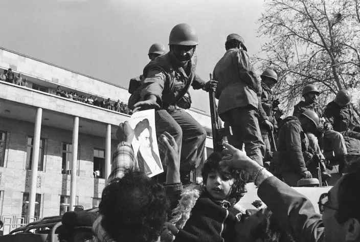 FILE - In this Jan. 15, 1979 file photo, a smiling Iranian soldier is hailed by demonstrators who decorated them with flowers and pictures of Ayatollah Ruhollah Khomeini, in Tehran, Iran. Wednesday, Jan. 16, 2019 marks the 40th anniversary of the shah abandoning his Peacock Throne and leaving his nation for the last time in his life, setting the stage for the country's 1979 Islamic Revolution only a month later. (AP Photo, File)