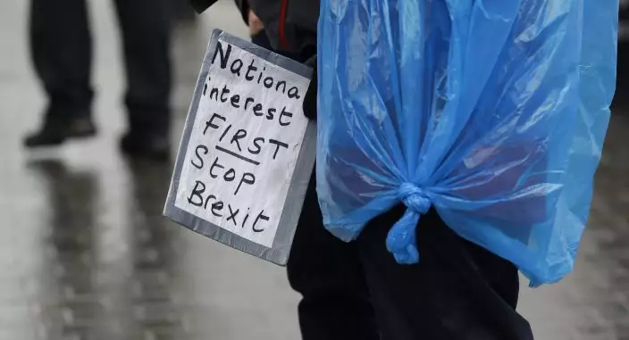 An anti-Brexit campaigner holds a banner as she shelters from the rain near parliament, in London, Tuesday, April 9, 2019. Prime Minister Theresa May has brought her case for a further delay to Britain's departure from the European Union to Berlin, while German and French officials are insisting that any extension to the deadline must come with strings attached and assurances from London. (AP PhotoKirsty Wigglesworth)