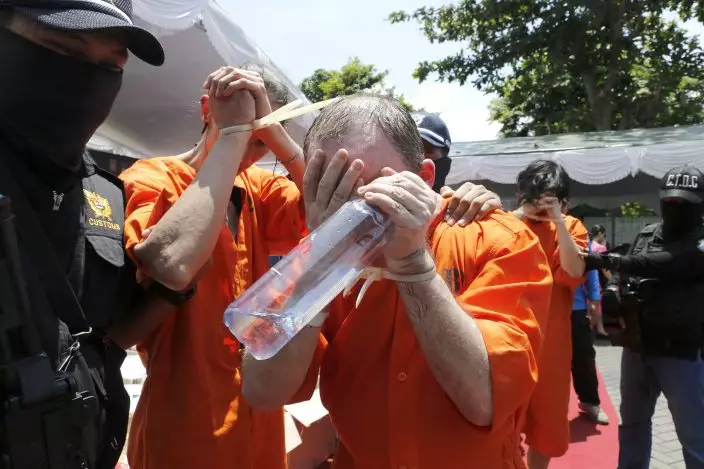 Foreign suspects detained for drugs charges are escorted by Indonesian custom officers during a press conference in Bali, Indonesia, Wednesday, Dec. 18, 2019. Indonesian authorities say they have arrested six foreigners for allegedly trying to smuggle drugs onto the tourist island of Bali. The foreigners, a Swiss man, a Thai man, a Singaporean woman, a Chilean man and two Hong Kong men, wearing orange detainees uniform were paraded with their feet and hands tied, at a news conference. (AP PhotoFirdia Lisnawati)