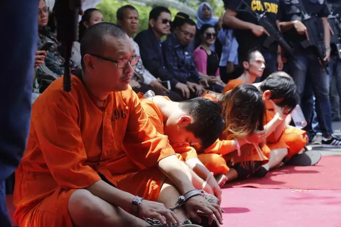 Foreign suspects detained for drugs charges sit during a press conference in Bali, Indonesia, Wednesday, Dec. 18, 2019. Indonesian authorities say they have arrested six foreigners for allegedly trying to smuggle drugs onto the tourist island of Bali. The foreigners, a Swiss man, a Thai man, a Singaporean woman, a Chilean man and two Hong Kong men, wearing orange detainees uniform were paraded with their feet and hands tied, at a news conference.(AP PhotoFirdia Lisnawati)