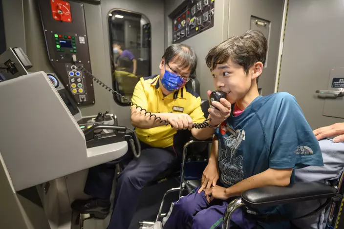 列車員工主任黃錦昌(左)向梓鍵遞上對講機， 讓梓鍵作車長廣播。